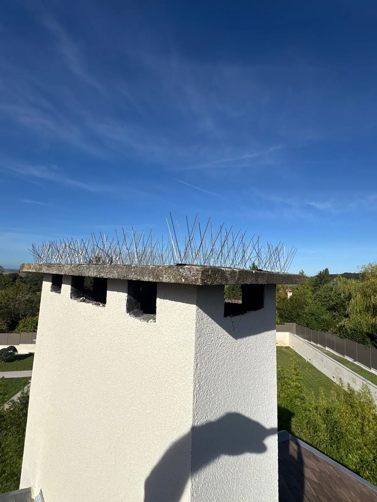 Souche de cheminée équipée de pics anti-pigeons en inox, sous un ciel bleu